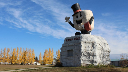 Image showing a large rock with a statue of a happy creature wearing a top hat on top of it.