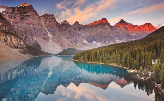 A view of Moraine Lake Banff National Park featuring a clear blue lake and tall mountains during sunset.