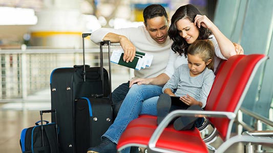 A couple with their daughter sitting on a bench waiting for their flight.