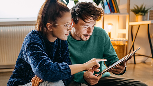 A couple sitting in their house looking at a tablet. 