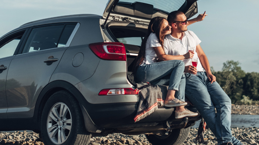 A couple sitting in the trunk of their grey SUV.