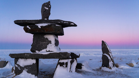 Black stone Inukshuk in arctic setting with dawn breaking in background.