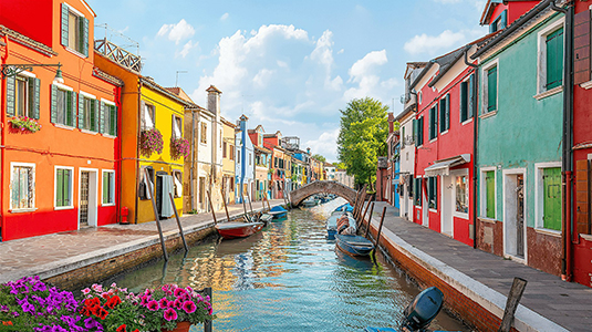 View of a canal on Burano island in Italy with small boats parked on its sides and colourful houses throughout the street.