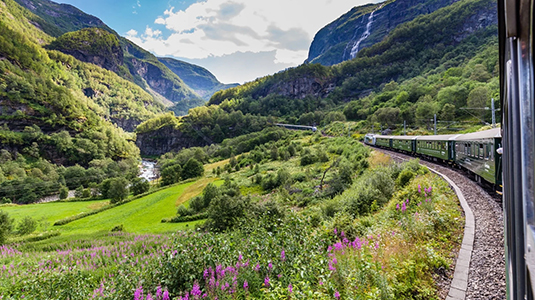 View from a side of a window of a moving train passing through valleys and mountsins. 