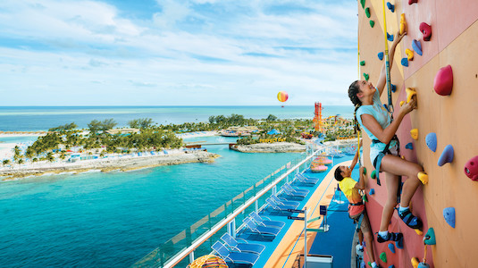 Two kids rock climbing on cruise ship with ocean views.