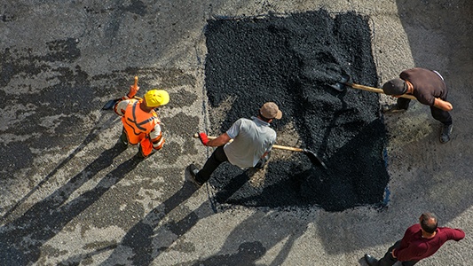 Four workers patching the road with asphalt.