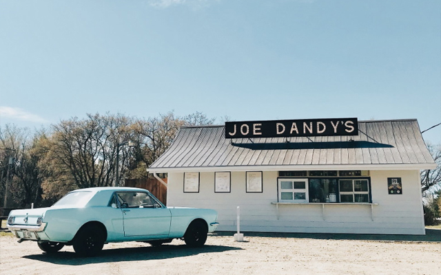 Image showing an exterior view of Joe Dandy's shop with a mid-1960's blue Ford Mustang parked out front.