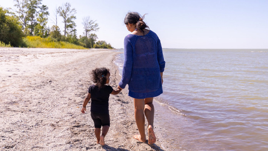 Image showing a woman and a small child walking barefooted on a beach.