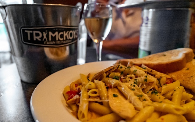 Image showing a cheesy plate of pasta in the foreground with an ice bucket and a glass of white wine on the table.
