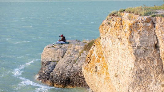 Image showing two people sitting on a blanket on a rocky shore looking out at the lake.