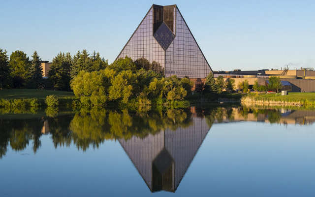 Image showing a pyramid-like building being reflected in a nearby pond.
